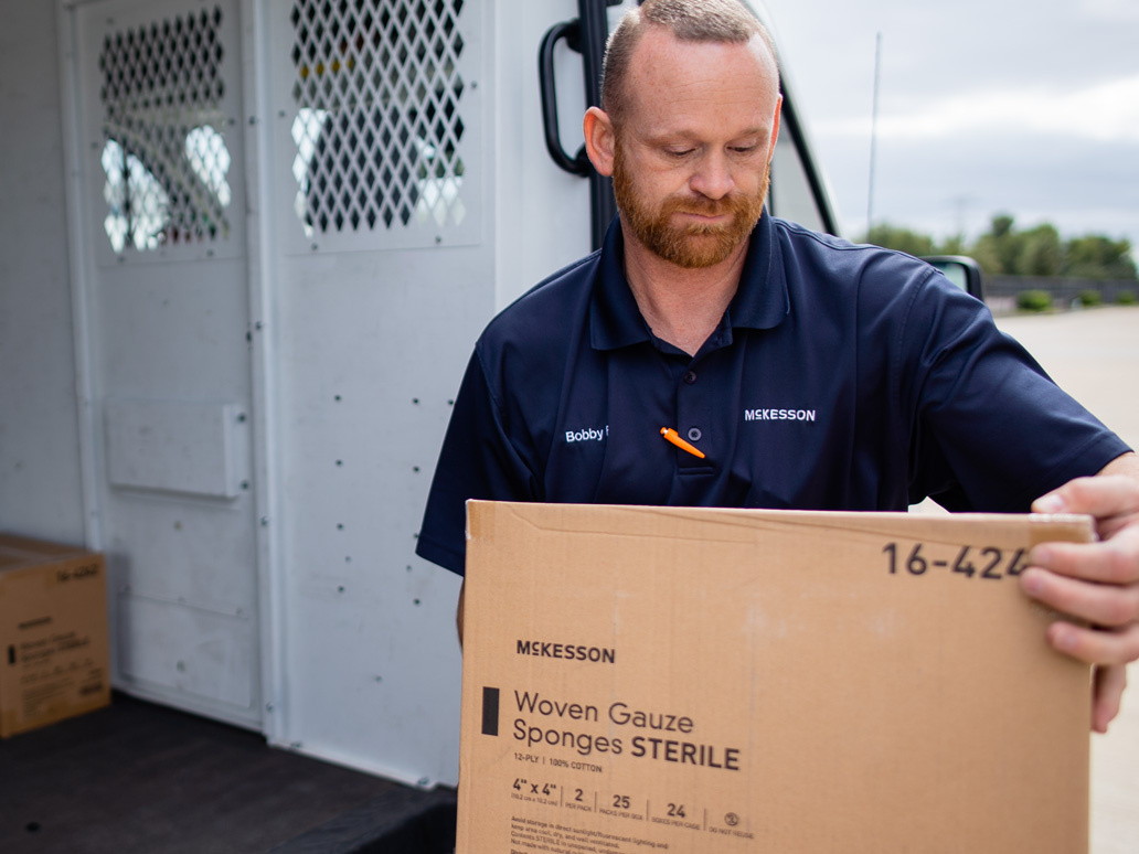 A McKesson delivery driver unloads a box from the back of a delivery truck.